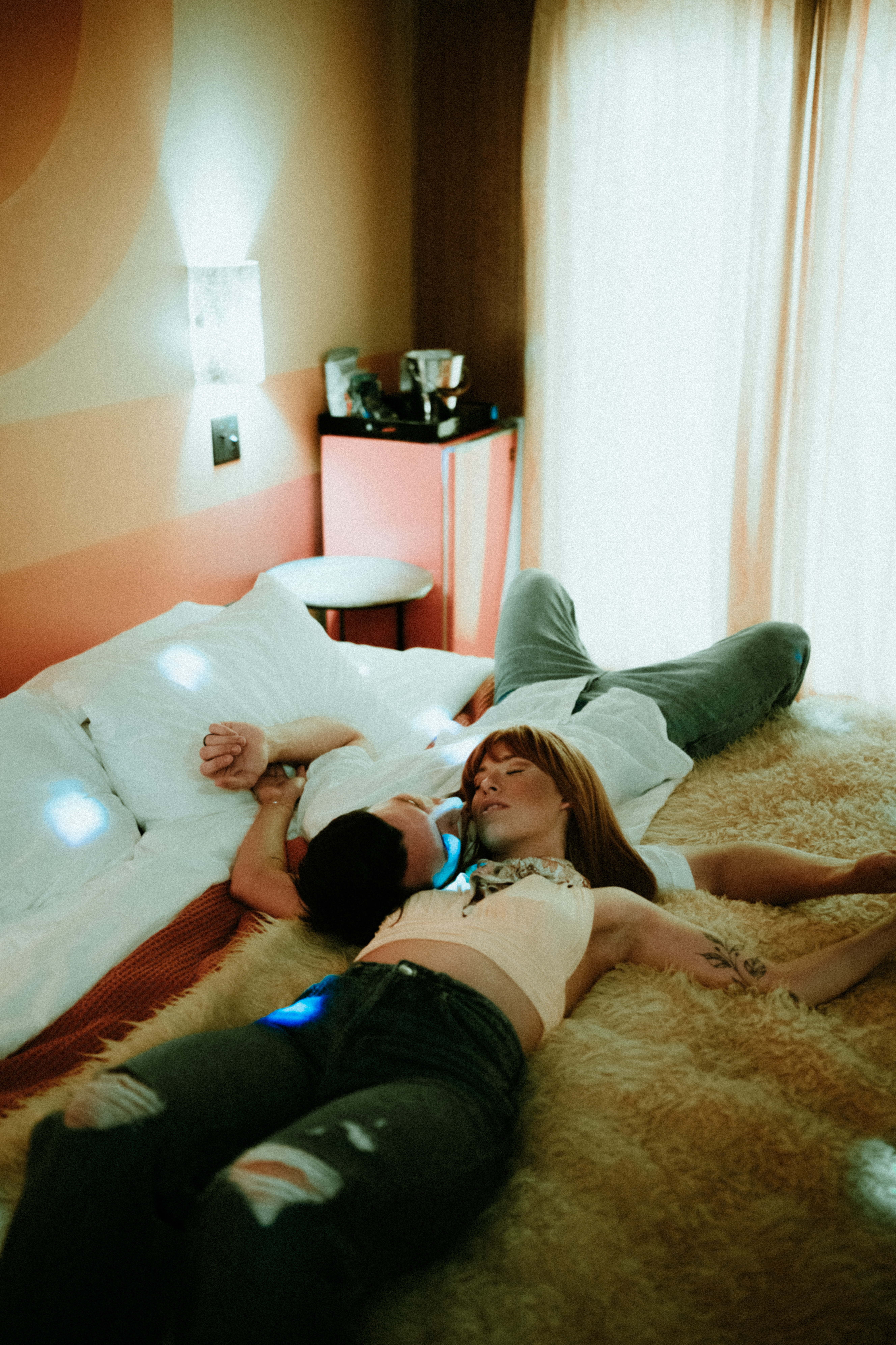 couple laying in 70s themed hotel room, shoulders and heads touching in opposite directions