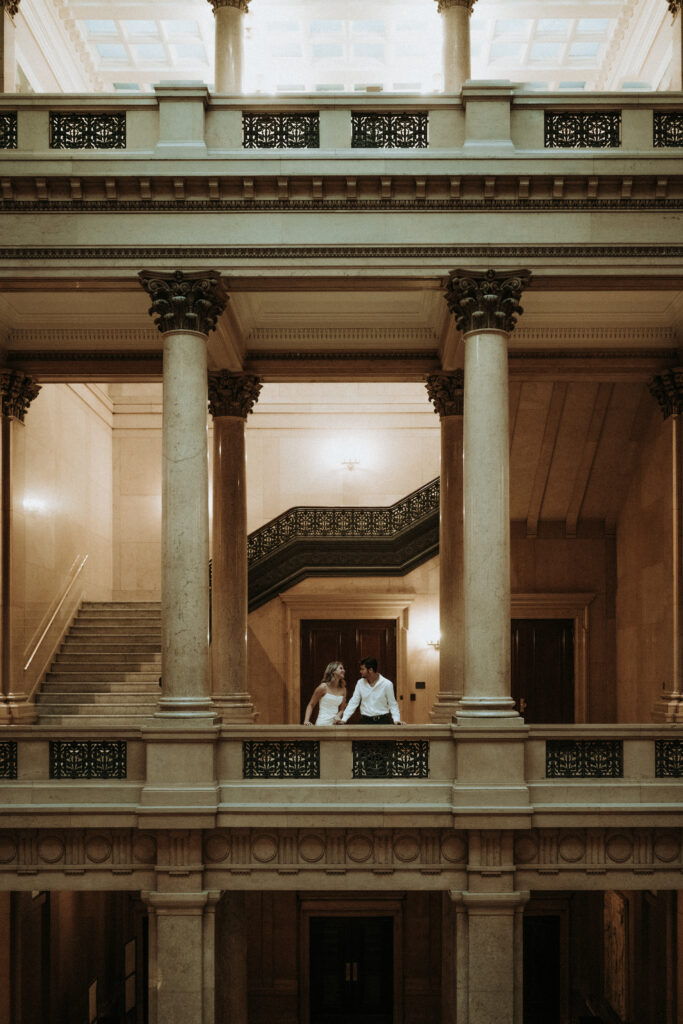 a photo of a couple kissing in between coulumns on the second floor of the carnegie art museum!